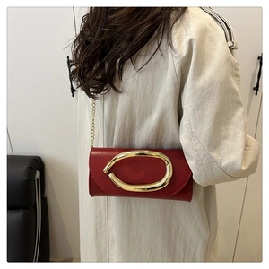 Detail of red leather crossbody bag with bold gold metal clasp and chain strap