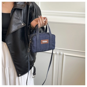 Detail of dark blue denim handbag with brown leather tag and adjustable crossbody strap