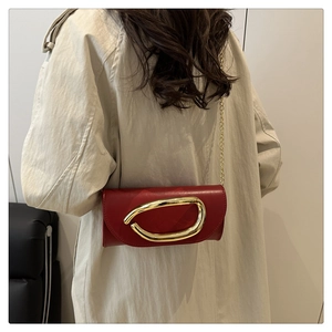 Close-up of red leather crossbody bag featuring a large gold oval buckle and chain