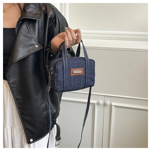 Detail shot of navy denim crossbody bag featuring white stitching and leather patch