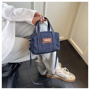 Detailed view of a vintage denim crossbody bag with contrast stitching and leather patch