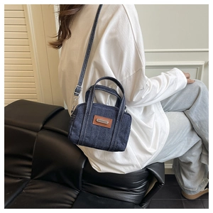 Detail of dark blue denim crossbody bag with contrast stitching and leather patch