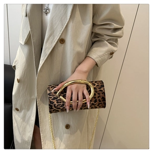 Detail of leopard print clutch with bold gold oval handle and chain worn with a trench coat