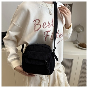 Detail of black corduroy crossbody bag featuring a front zip pocket and woven zipper pull