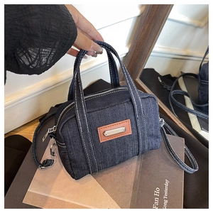 Detail of vintage denim bowling bag featuring white contrast stitching and leather tag