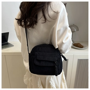 Close-up of black corduroy shoulder bag showing ribbed texture and woven zipper pull