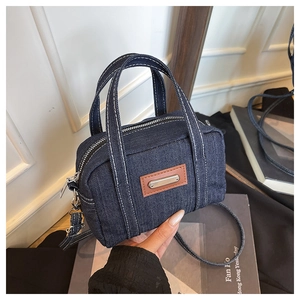 Detailed close-up of dark blue denim handbag with white stitching and metal logo plate