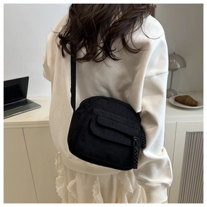 Macro detail of black corduroy crossbody bag featuring a textured flap pocket and zipper cord