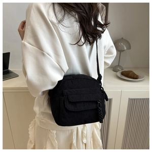 Close-up of black corduroy crossbody bag with tassel detail worn in cozy indoor setting