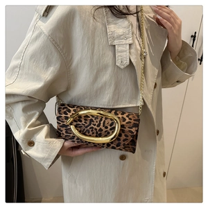 Detail of leopard print chain bag featuring a large gold oval buckle on beige coat