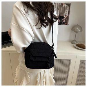 Detail of black corduroy crossbody bag with woven zipper pull and front flap pocket