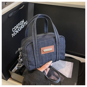 Detailed view of dark blue denim handbag with white contrast stitching and brown leather trim