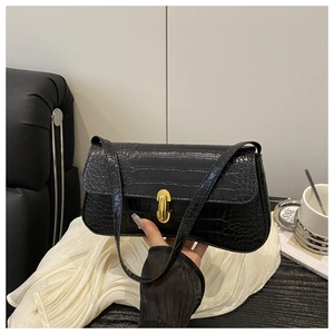 Detail of black faux crocodile skin texture and gold metal buckle on baguette shoulder bag