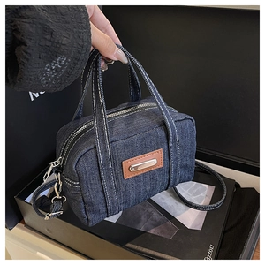 Detailed close-up of dark blue denim boston bag showing contrast white stitching and leather patch