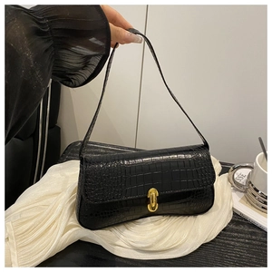 Detail of black baguette bag with faux crocodile texture and gold metal buckle