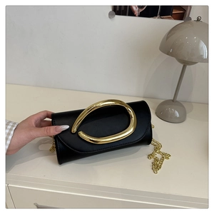Close-up of black leather box clutch featuring a bold gold metal ring and chain strap