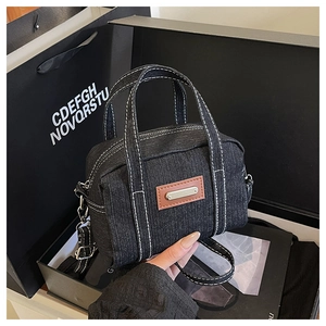 Detail of black denim mini handbag with contrast stitching and leather tag on dark background
