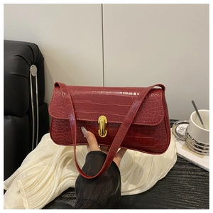 Detail of red crocodile texture baguette bag with golden metal twist lock and slim strap
