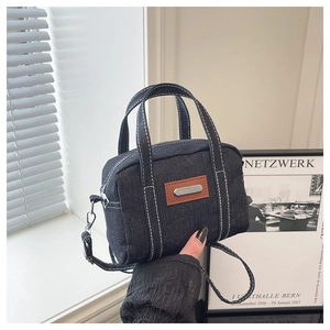 Macro detail of navy denim pillow bag with white stitching and leather brand tag