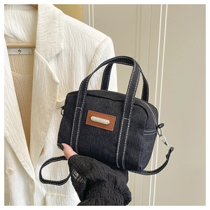 Detail view of black denim handbag featuring white contrast stitching and brown leather patch