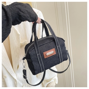 Detail of black denim handbag with contrast stitching and brown leather logo patch