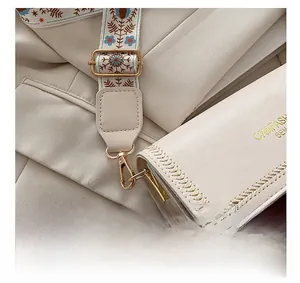 Detail of embroidered bohemian wide strap and gold hardware on cream shoulder bag