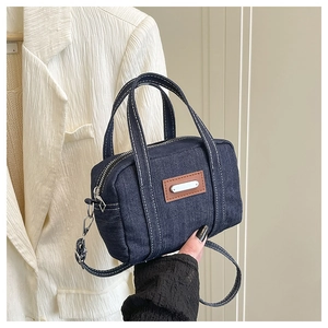 Close-up of small blue denim Boston bag with contrast white stitching and brown leather patch