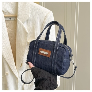 Detail of navy denim boston bag with contrast stitching and leather trim held by model