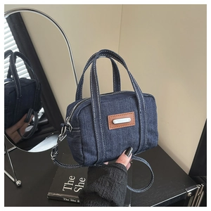 Detailed close-up of dark blue denim tote bag with white stitching and leather patch