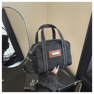 Close-up of black denim handbag with contrast white stitching and metal logo detail
