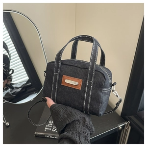 Close-up of small denim tote bag with white contrast stitching and brown leather patch