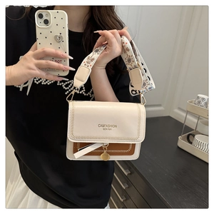 Detail of crossbody bag with wide ethnic strap and gold pendant on contrast flap