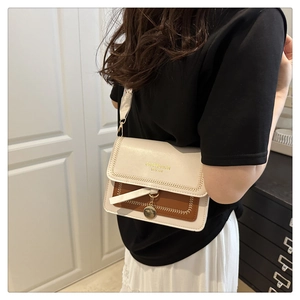 Detail of two-tone crossbody bag featuring golden round charm and stylish wide strap