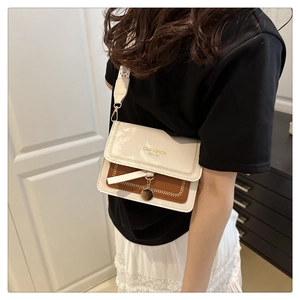 Close-up of contrast crossbody bag featuring white flap with gold text and vintage strap