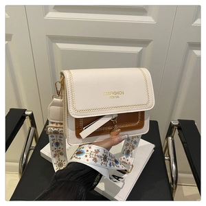 Detail of wide embroidered shoulder strap and wave stitching on a two-tone crossbody bag