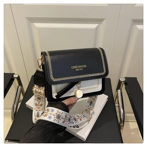 Detail of crossbody bag featuring a wide ethnic embroidery strap and gold-tone pendant