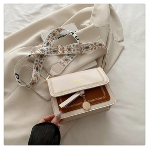 Detail of a chic cream and brown crossbody bag with decorative wide strap and gold hardware