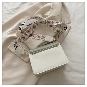 Close-up of wide ethnic embroidered strap and contrast flap on the white leather bag