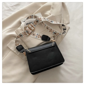 Close-up of black crossbody bag with floral embroidery wide strap on a white blazer