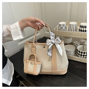 Detail of beige canvas tote with leather trim, mini charm bag and decorative silk scarf