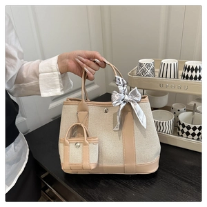 Detail of beige canvas tote bag with khaki leather trim, silk scarf, and mini charm