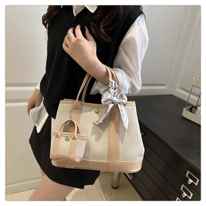 Detail of canvas tote bag with brown leather handles, silk scarf and mini bag charm