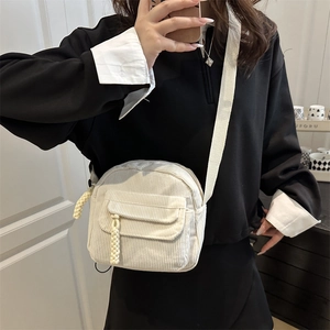 Minimalist beige corduroy crossbody bag with woven zipper pull and front pocket