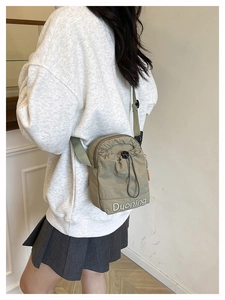 Gros plan sur un sac bandoulière en nylon kaki avec cordon de serrage et broderie blanche