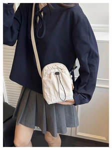 Détail du sac bandoulière crème avec cordon, logo brodé et bandoulière en nylon