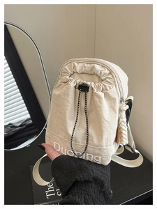 Détail macro du sac bandoulière beige en nylon avec plis à cordon et broderie blanche