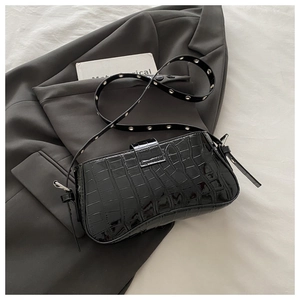 Close-up of black crocodile pattern baguette bag with silver eyelet strap on grey suit