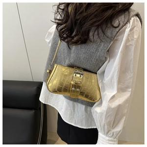 Detail of gold crocodile embossed shoulder bag featuring oversized metal buckle accents