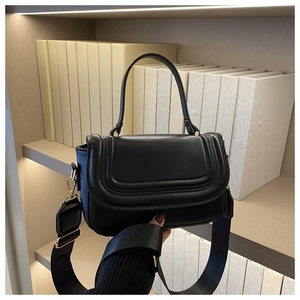 Detail of black crossbody bag with textured leather flap and wide adjustable strap