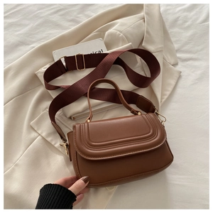 Detailed close-up of brown leather crossbody bag with wide strap on elegant fabric